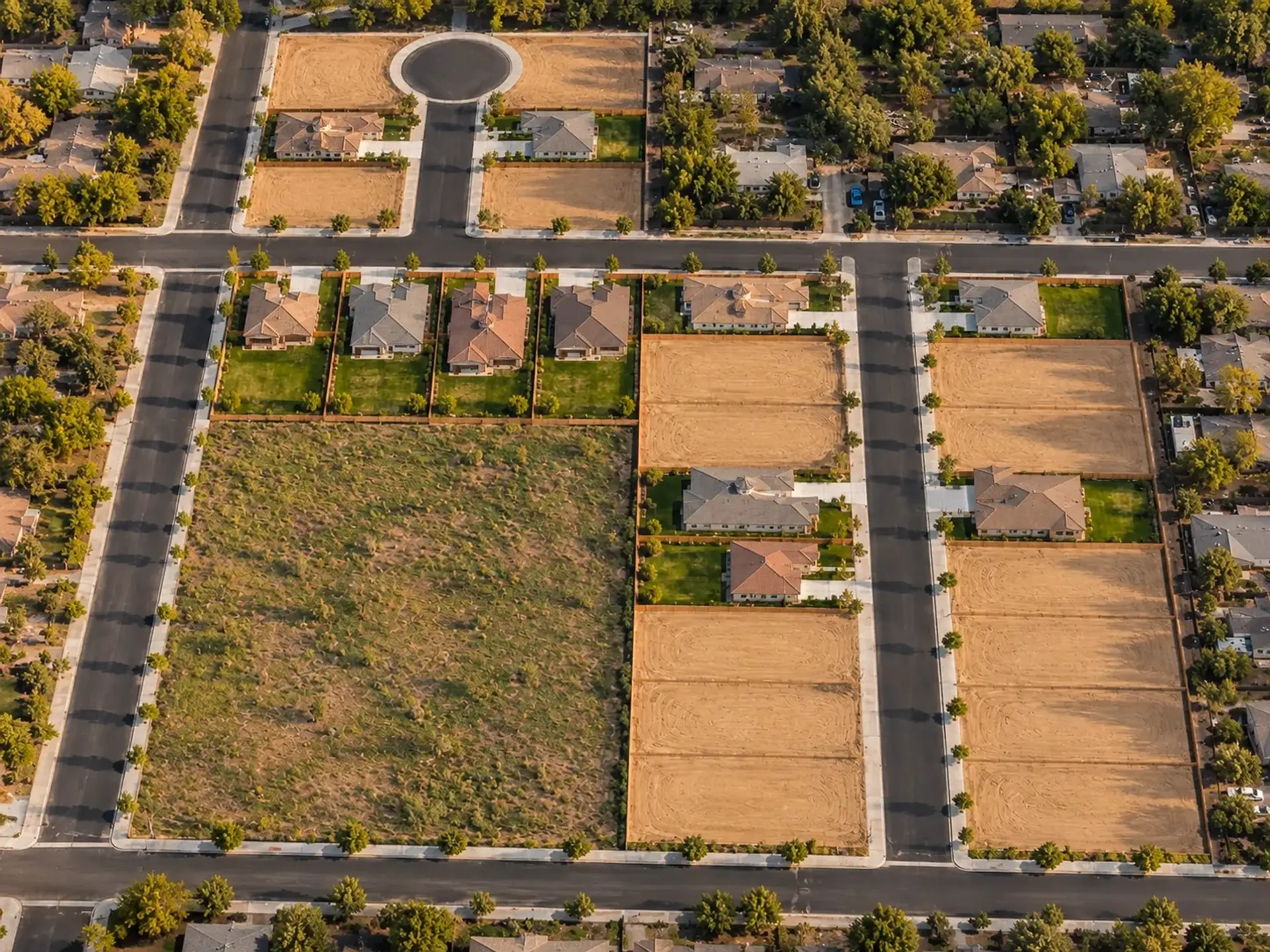 Aerial rendering of a new 26-lot community from a drone: a central street with graded lots and new single-story homes on both sides, four homes in a row along a cross street, and a cul-de-sac at the back, set in an older tree-lined neighborhood.